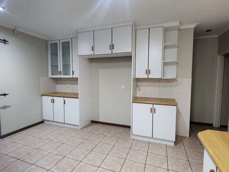 A clean, empty kitchen featuring white built-in cabinetry, laminate countertops, and neutral tiled flooring, offering a functional space ready for personalization.
