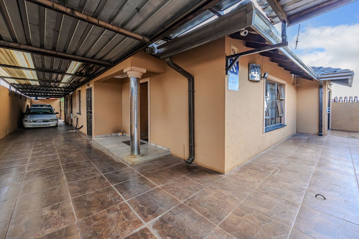 A covered patio area with tiled flooring and a corrugated metal roof structure, providing a functional outdoor space along the side of the house.