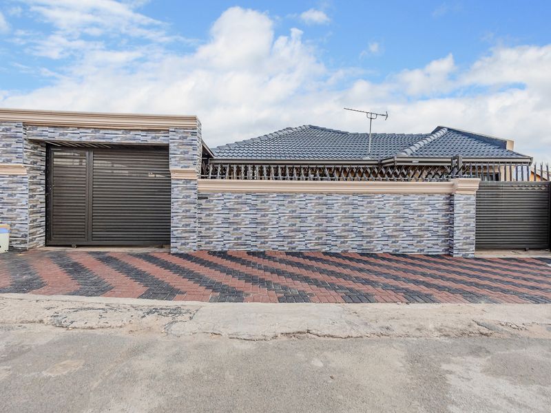 Front elevation featuring a modern tiled boundary wall, secure metal gates, and a patterned paved driveway leading to the property entrance.