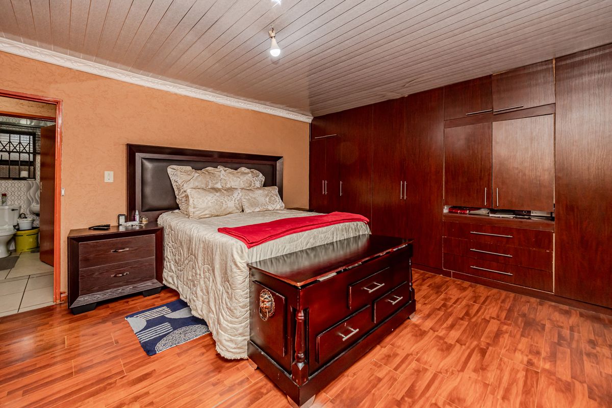 Spacious bedroom featuring extensive built-in wooden cabinetry, laminate flooring, and a unique timber-paneled ceiling with coving.