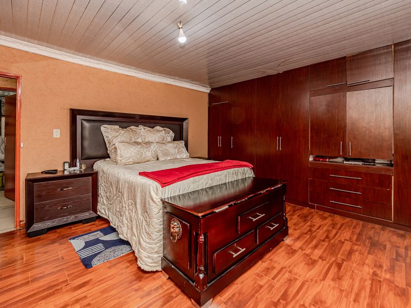 Spacious bedroom featuring extensive built-in wooden cabinetry, laminate flooring, and a unique timber-paneled ceiling with coving.