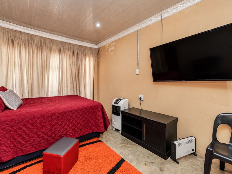 A bedroom featuring a tongue and groove ceiling with decorative cornice and wall-mounted television, showing signs of wall surface deterioration.