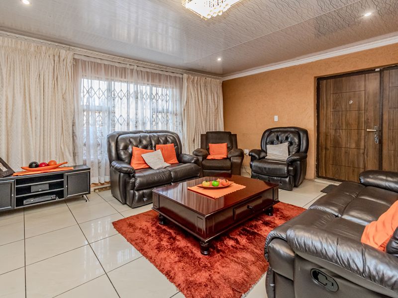 A spacious living room featuring tiled flooring, textured ceiling finishes, and a secure entrance door, providing a comfortable and functional family living space.