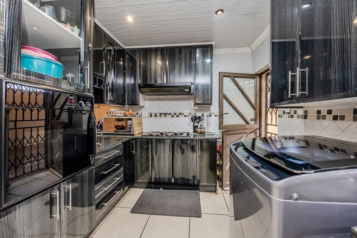 A modern kitchen featuring dark wood-grain cabinetry, granite countertops, built-in oven, extractor fan, and tiled finishes throughout.