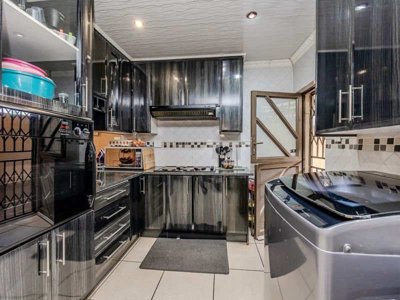 A modern kitchen featuring dark wood-grain cabinetry, granite countertops, built-in oven, extractor fan, and tiled finishes throughout.