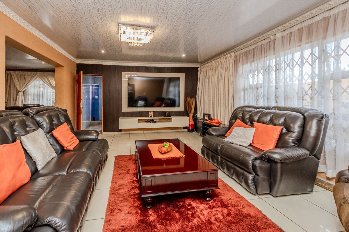 A spacious living room featuring tiled flooring, a built-in media wall, and decorative ceiling finishes with recessed lighting.