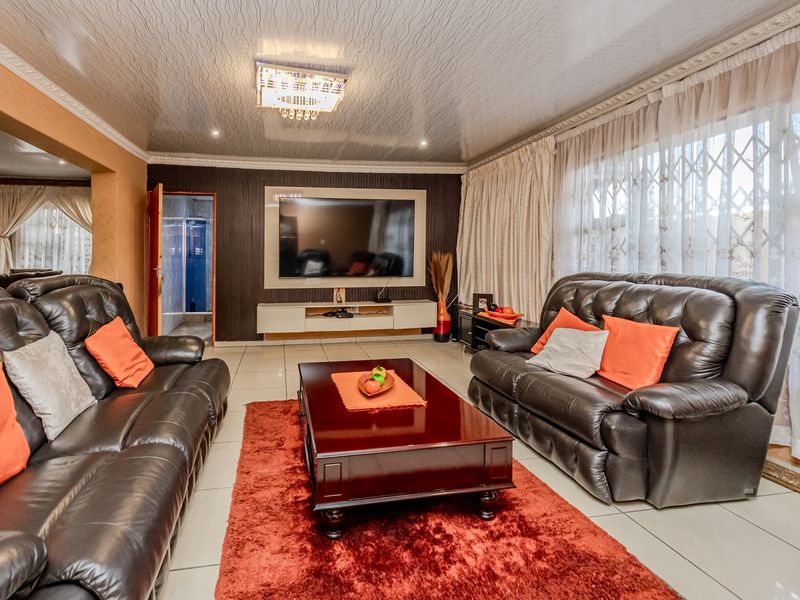 A spacious living room featuring tiled flooring, a built-in media wall, and decorative ceiling finishes with recessed lighting.