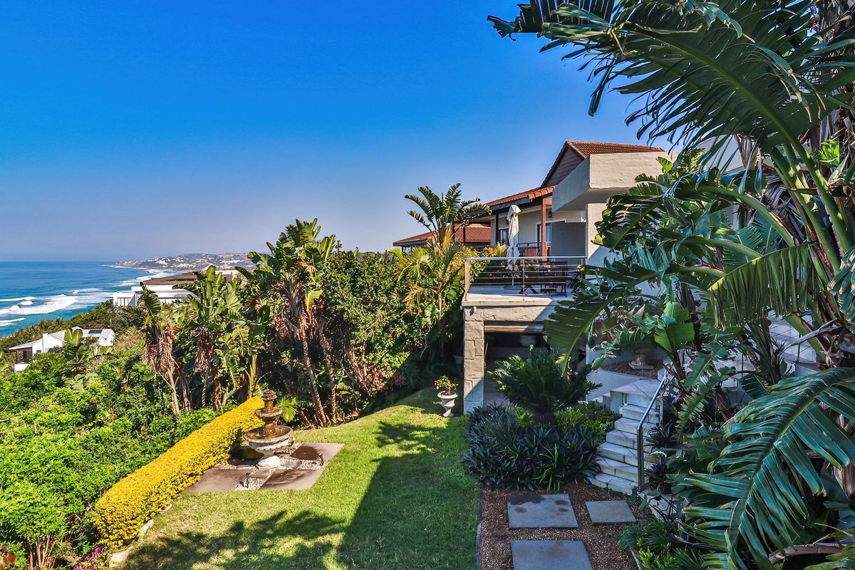 A scenic rear exterior view featuring a landscaped garden, stone fountain, and a balcony overlooking the ocean.