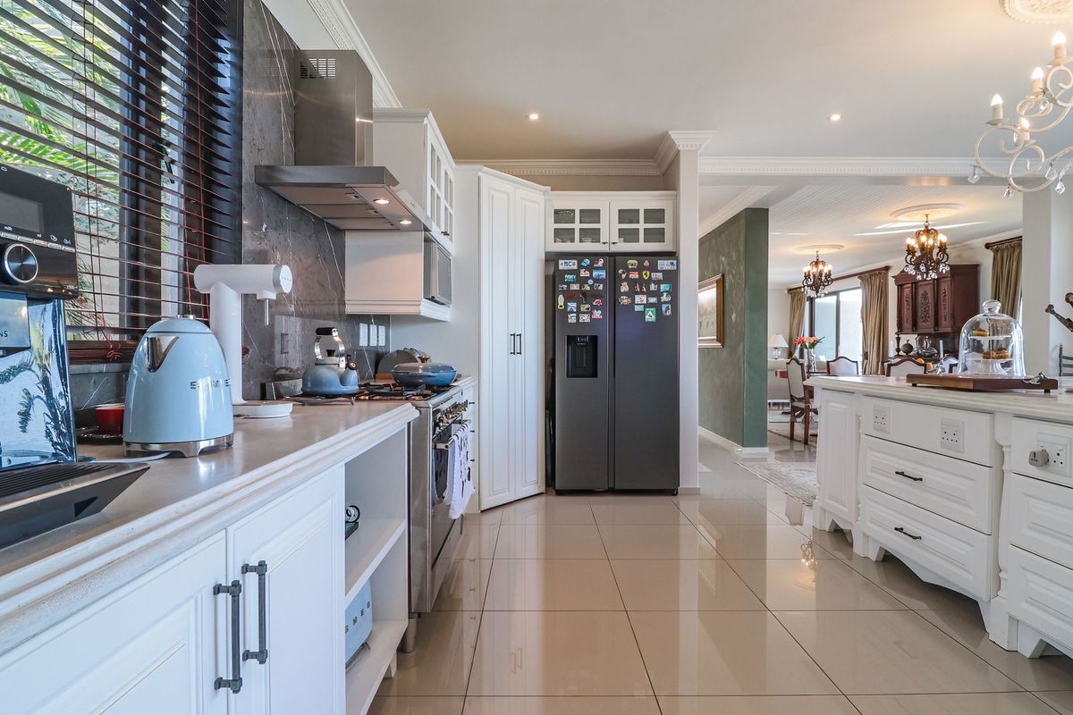 A well-appointed kitchen featuring stone countertops, white cabinetry, a central island, and high-end finishes, seamlessly flowing into the adjacent dining area.