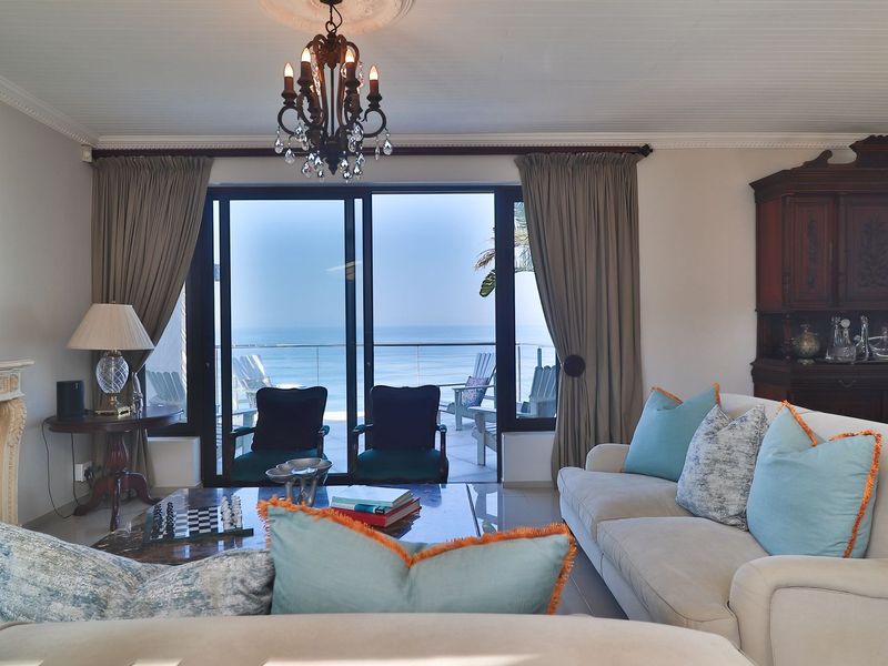 Spacious living room featuring a classic fireplace, elegant chandelier, and large sliding glass doors opening to a scenic ocean view.