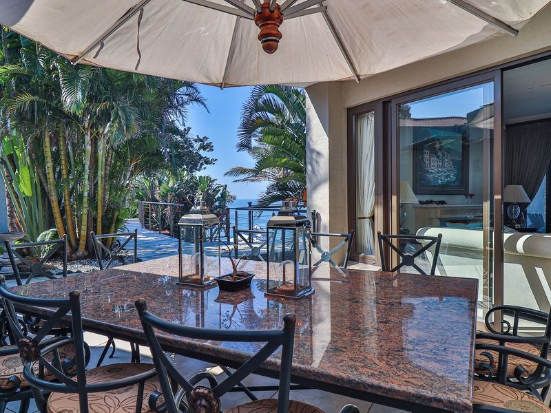 A spacious covered patio featuring tiled flooring and large sliding glass doors, offering a seamless transition to the outdoor garden and ocean view.