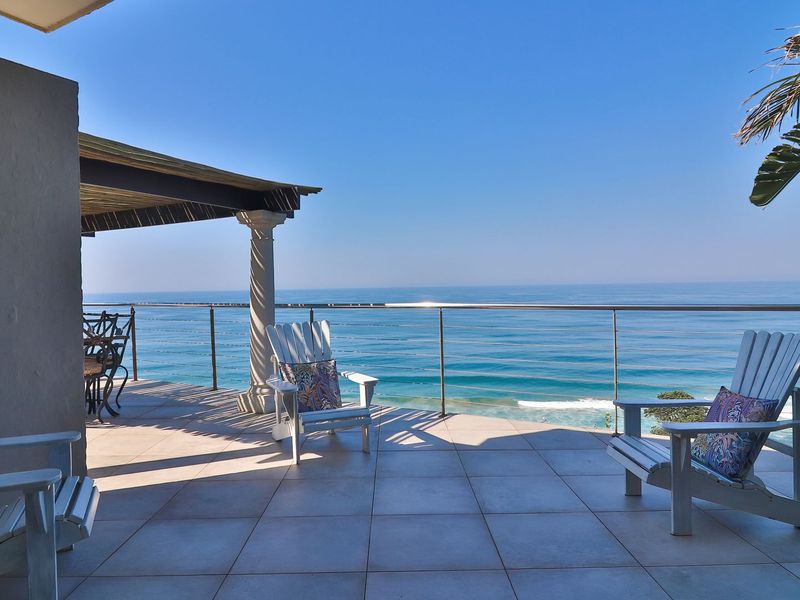 Spacious covered balcony featuring tiled flooring, a decorative column, and a stainless steel balustrade, offering expansive ocean views.