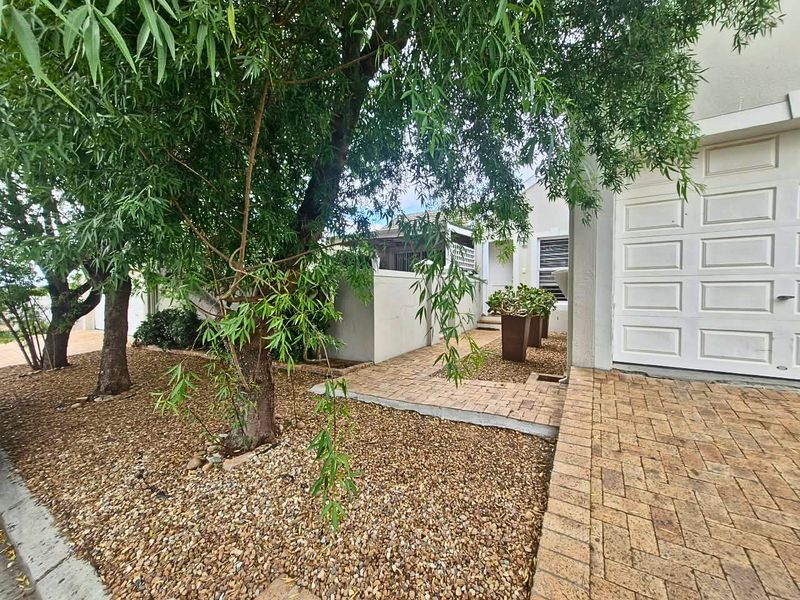 Front exterior view of the property featuring a brick paved driveway, garage access, and established garden landscaping with mature trees.