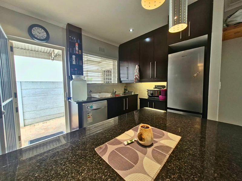 A functional kitchen featuring dark cabinetry, granite countertops, and integrated lighting, with direct access to an outdoor patio area.
