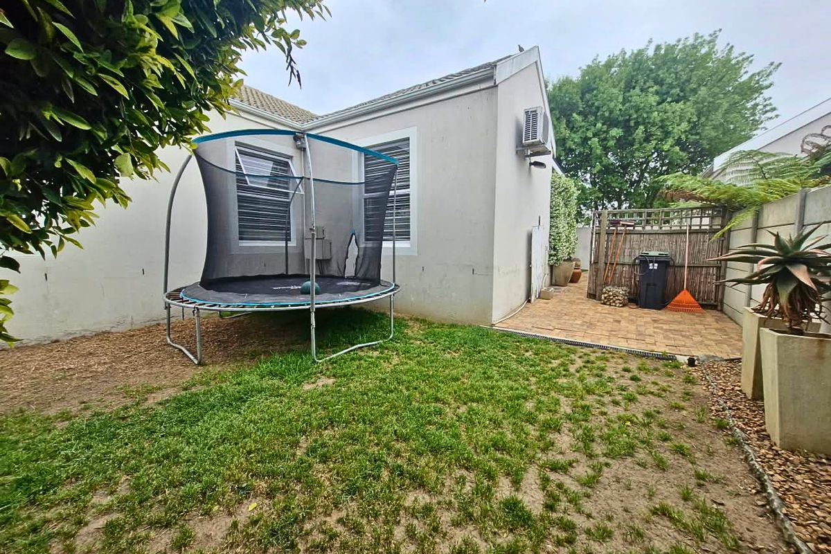 Rear garden area featuring a paved patio, lawn space, and wall-mounted air conditioning unit.