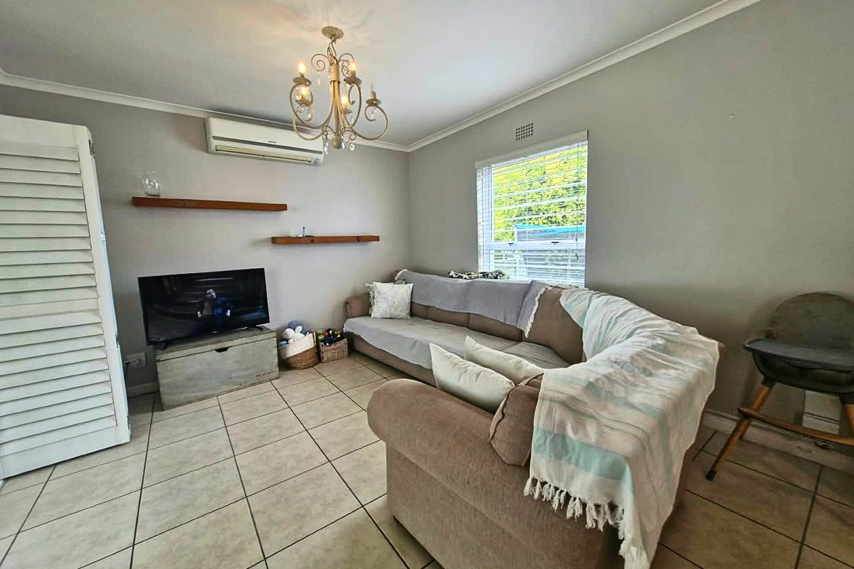 A comfortable living room featuring ceramic tiled flooring, a wall-mounted split-system air conditioner, and floating shelving, providing a functional and well-maintained living space.