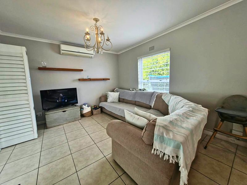 A comfortable living room featuring ceramic tiled flooring, a wall-mounted split-system air conditioner, and floating shelving, providing a functional and well-maintained living space.