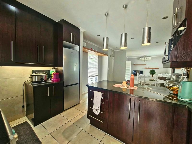 Modern open-plan kitchen featuring dark wood cabinetry, granite countertops, a central island, and stylish pendant lighting, seamlessly flowing into the dining area.
