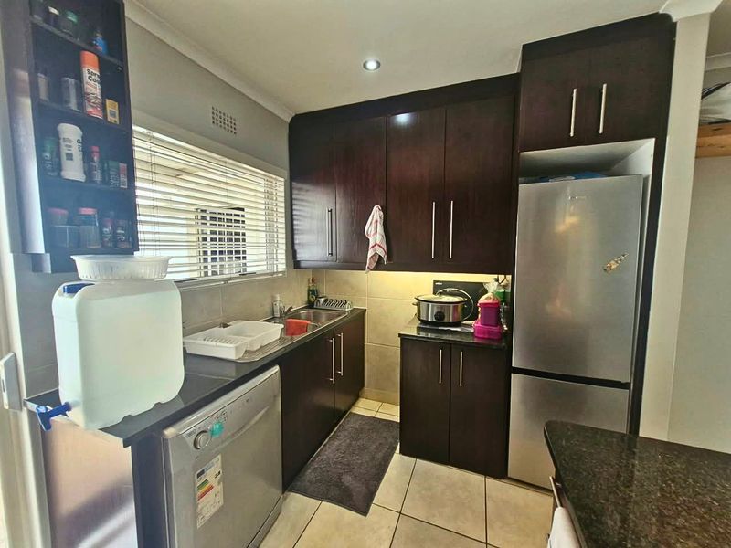 A functional kitchen featuring dark wood cabinetry, granite countertops, stainless steel sink, and tiled flooring with integrated appliance spaces.