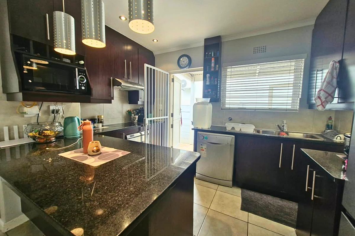 Modern kitchen featuring dark wood cabinetry, granite countertops, stainless steel sink, and integrated appliances with direct access to an outdoor area.
