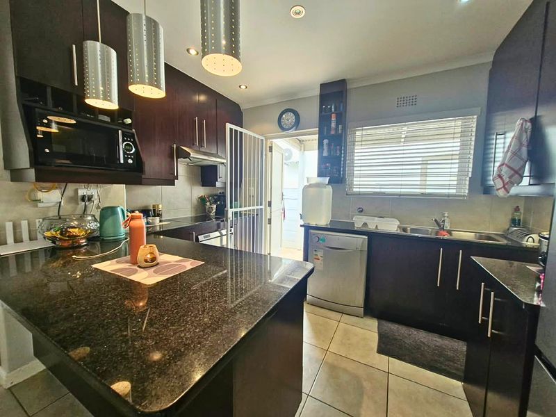 Modern kitchen featuring dark wood cabinetry, granite countertops, stainless steel sink, and integrated appliances with direct access to an outdoor area.