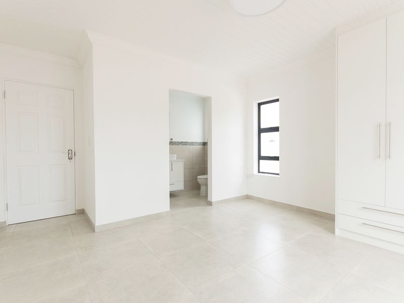 A bright, modern, and empty bedroom featuring neutral tiled flooring, built-in cupboards, and direct access to an en-suite bathroom.
