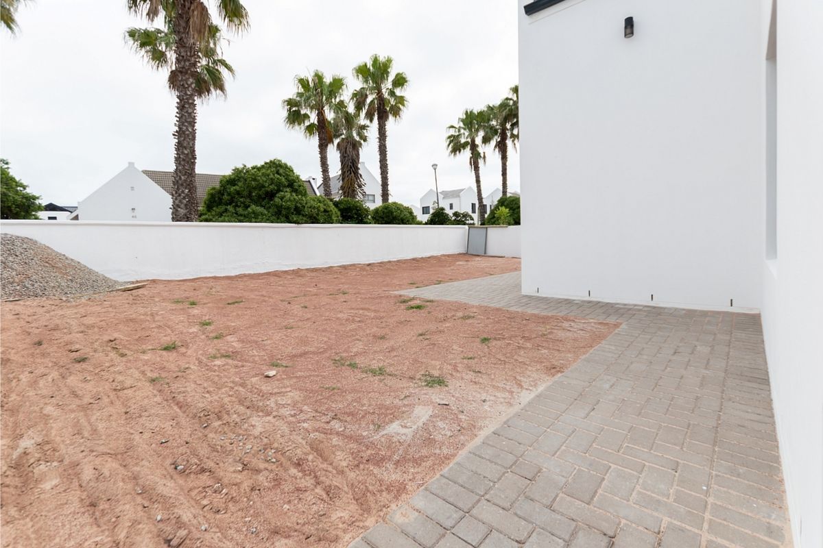 A rear exterior view featuring a paved patio area and an unlandscaped garden space enclosed by a boundary wall.