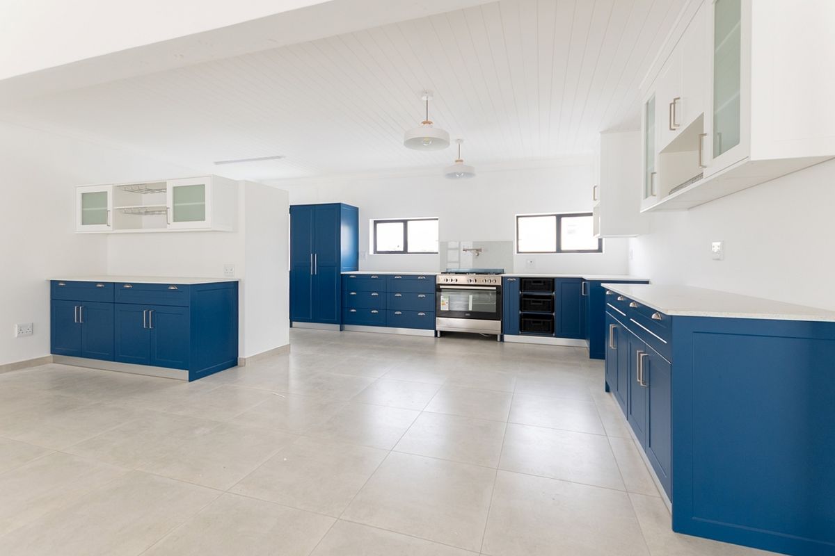 Spacious, modern kitchen featuring vibrant blue cabinetry, stone countertops, integrated appliances, and neutral tiled flooring in a bright, open-plan layout.