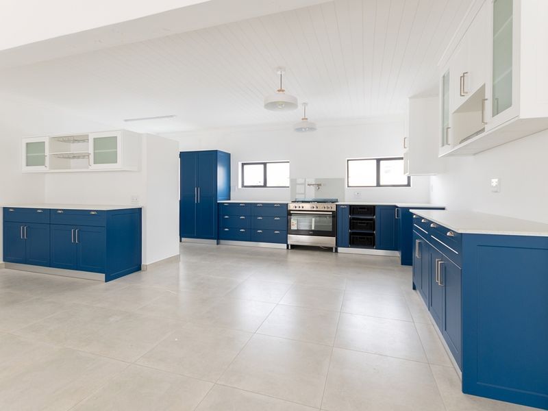 Spacious, modern kitchen featuring vibrant blue cabinetry, stone countertops, integrated appliances, and neutral tiled flooring in a bright, open-plan layout.