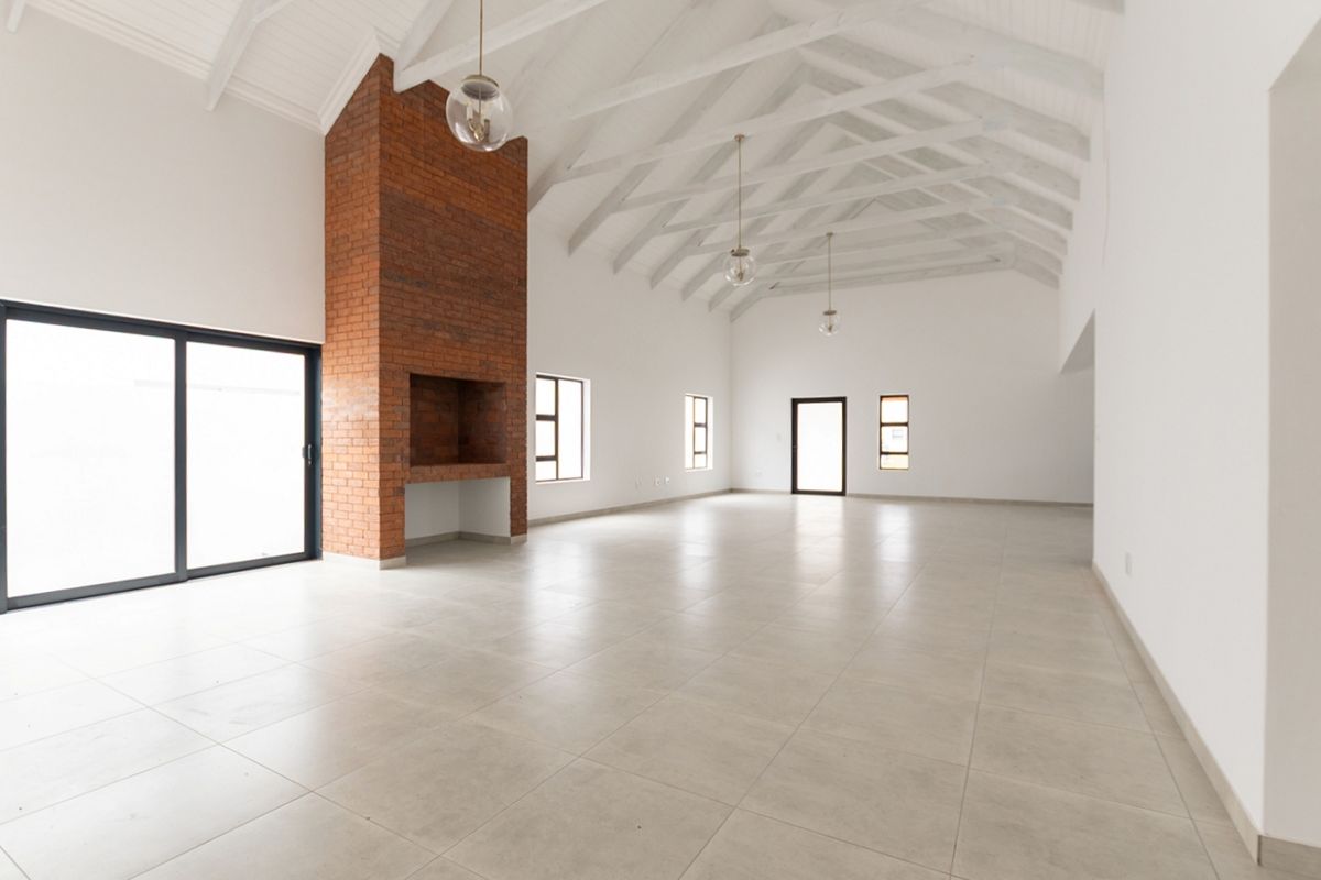 Spacious open-plan living area featuring a striking exposed brick fireplace, vaulted ceilings with white trusses, and large sliding doors leading to the exterior.