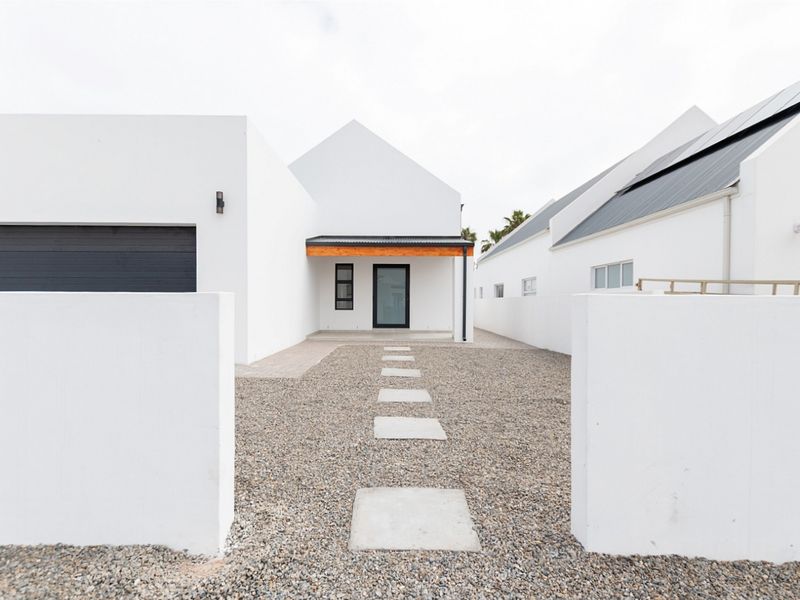 Modern minimalist front facade featuring a clean white exterior, gravel driveway with stone pavers, and a covered entrance with timber detailing.