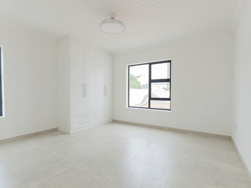 A bright, empty bedroom featuring neutral tiled flooring, built-in cupboards, and a tongue and groove ceiling with modern aluminium window frames.