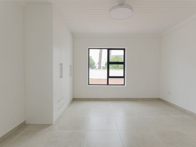 A bright, modern, and empty bedroom featuring neutral tiled flooring, built-in cupboards, and a clean, minimalist aesthetic.