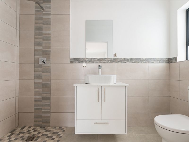 Modern bathroom featuring a walk-in shower with decorative tile accents, a floating vanity with a vessel sink, and neutral wall tiling.
