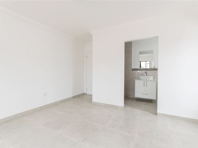 A bright, empty bedroom featuring neutral tiled flooring and an open-plan en-suite bathroom with a modern vanity and vessel sink.