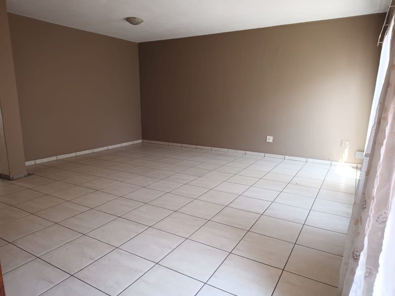 A spacious, empty living area featuring neutral-toned walls and light-colored ceramic floor tiles, providing a blank canvas for interior design.