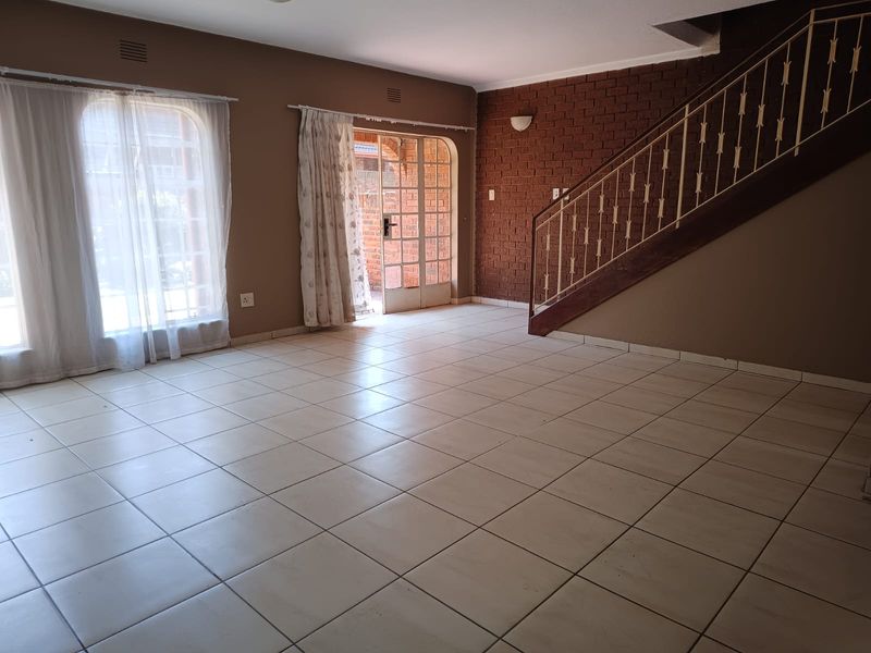 Spacious living area featuring tiled flooring, an exposed brick feature wall, and a staircase with a metal balustrade, leading to an outdoor patio area.