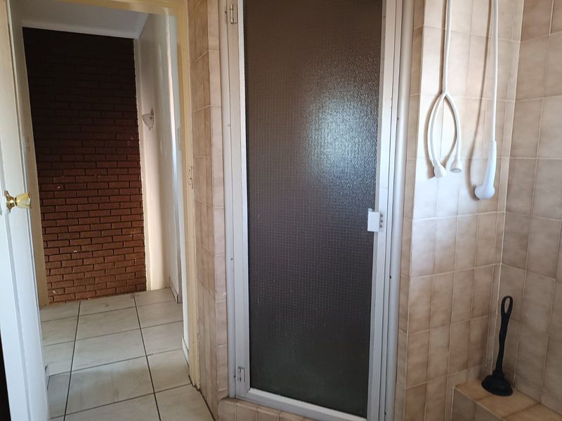 A dated bathroom featuring tiled walls and flooring with a built-in shower enclosure, requiring cosmetic updates to modernize the space.