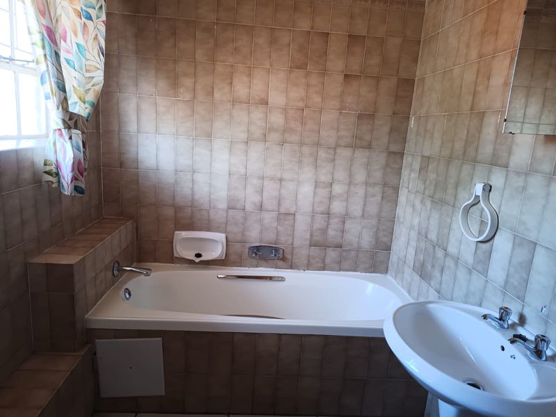 A functional bathroom featuring a built-in bathtub, pedestal washbasin, and full-height ceramic wall tiling in a neutral tone.