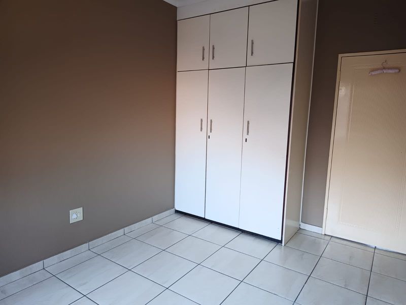 A clean, empty bedroom featuring neutral wall tones, white tiled flooring, and ample built-in cupboard storage space.