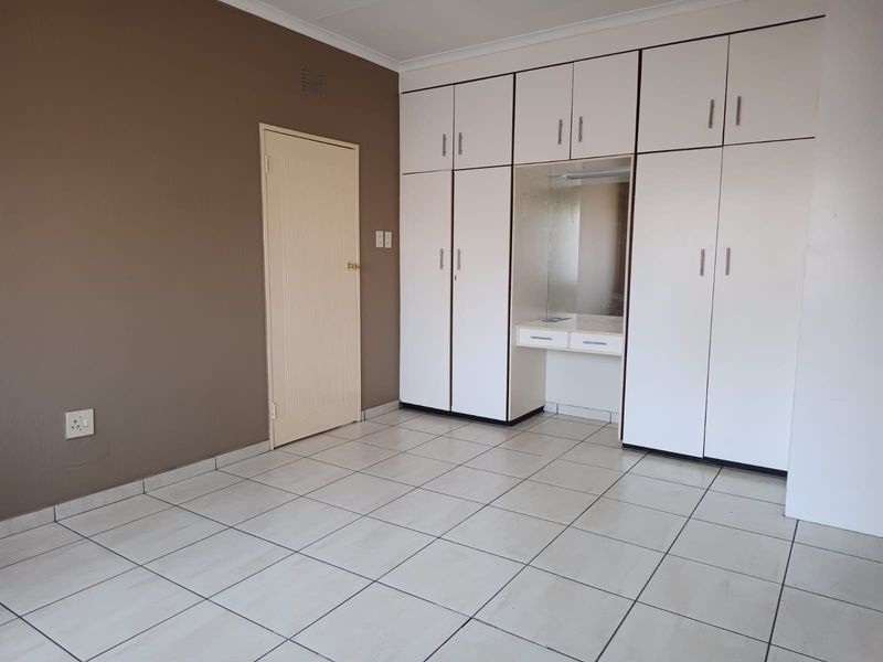 A spacious, empty bedroom featuring neutral tiled flooring and extensive built-in white cabinetry with an integrated vanity area.