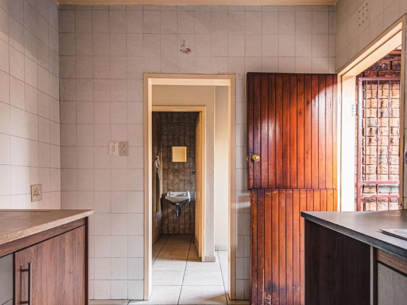 A functional scullery area featuring tiled walls, built-in cabinetry with laminate countertops, and a stainless steel sink, leading through to an adjacent utility space.