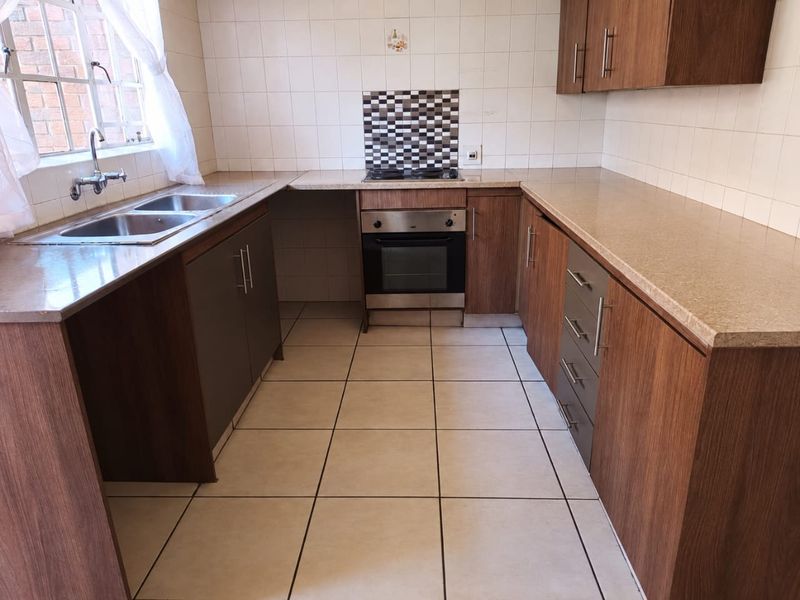 A functional kitchen featuring wood-look cabinetry, laminate countertops, a built-in oven and hob, and tiled flooring throughout.