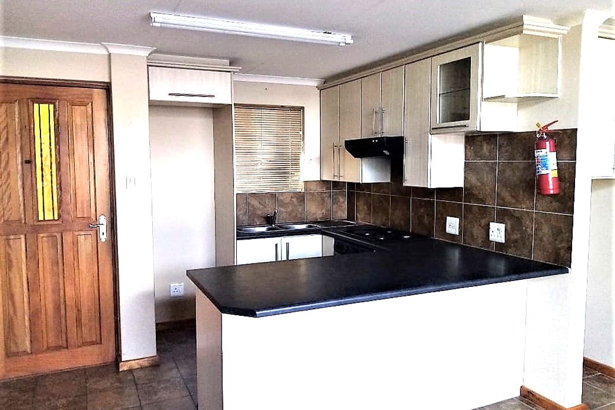 A functional kitchen featuring built-in cabinetry, dark laminate countertops, a tiled backsplash, and a breakfast bar, finished with tiled flooring.