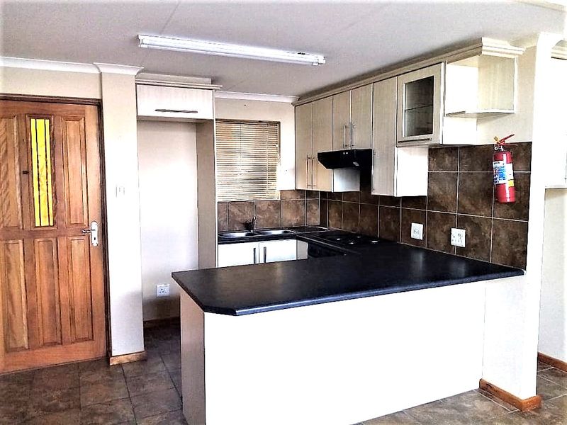 A functional kitchen featuring built-in cabinetry, dark laminate countertops, a tiled backsplash, and a breakfast bar, finished with tiled flooring.