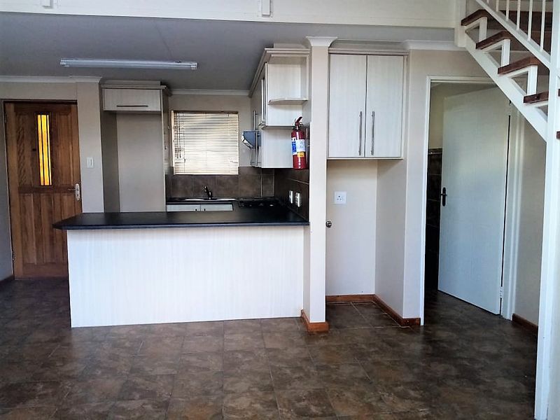 Open plan kitchen area featuring built-in cabinetry, a breakfast counter, and tiled flooring, with an adjacent staircase leading to the upper level.
