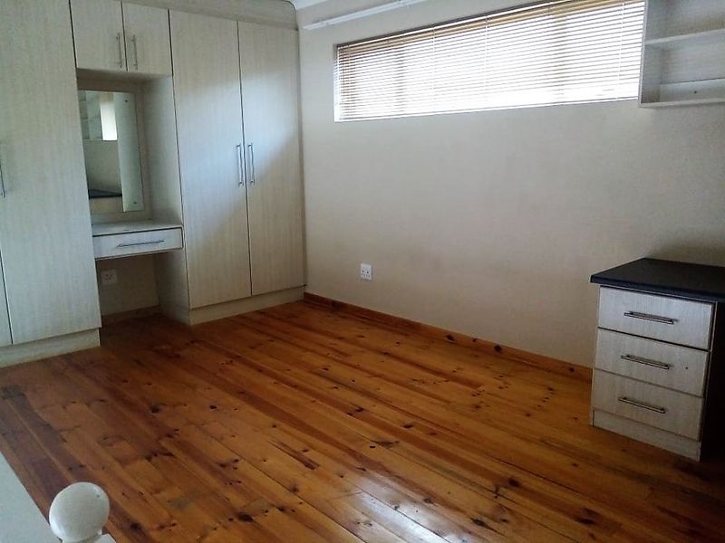 A spacious bedroom featuring polished timber flooring, extensive built-in cupboards with an integrated vanity, and horizontal window blinds.