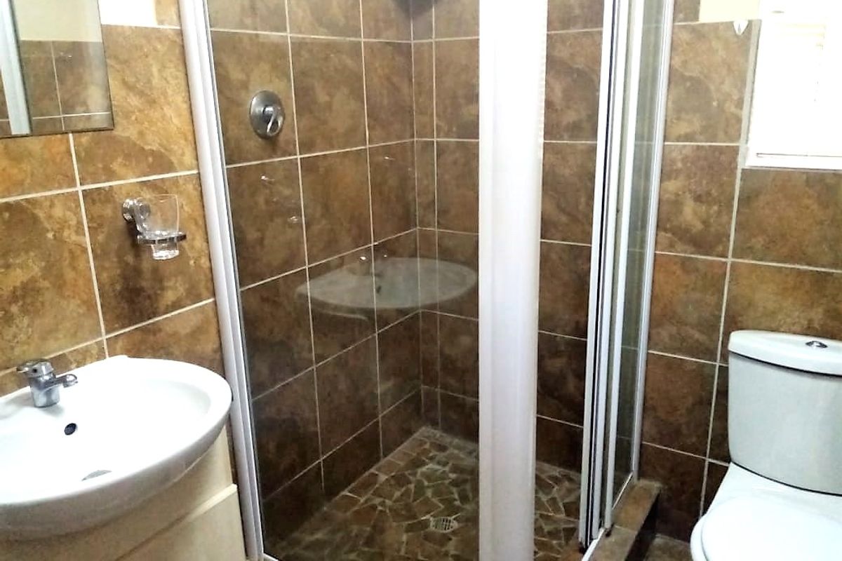 A functional bathroom featuring a shower enclosure, vanity basin, and toilet with brown tiled finishes throughout.