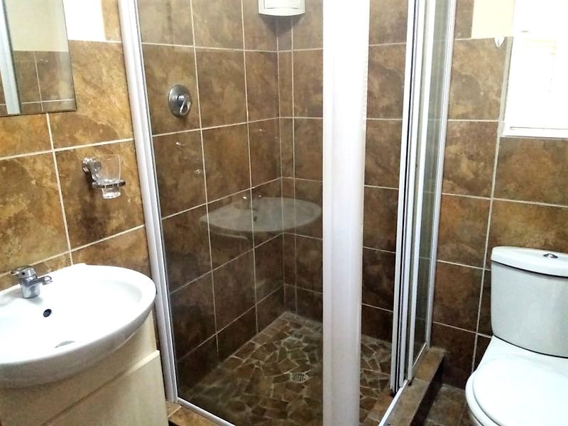 A functional bathroom featuring a shower enclosure, vanity basin, and toilet with brown tiled finishes throughout.