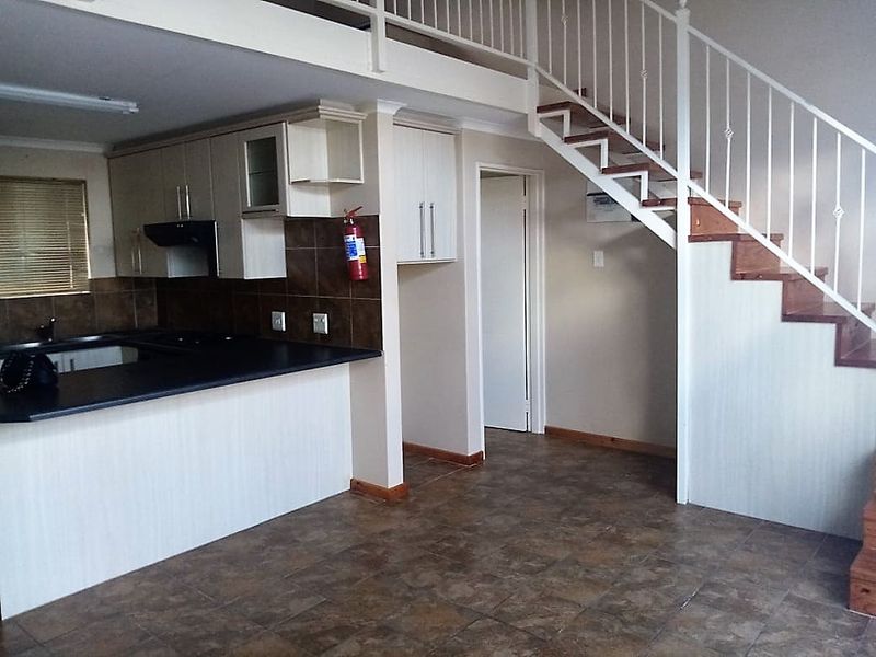 Open plan kitchen area featuring built-in cabinetry, tiled backsplash, and a staircase leading to a mezzanine level.